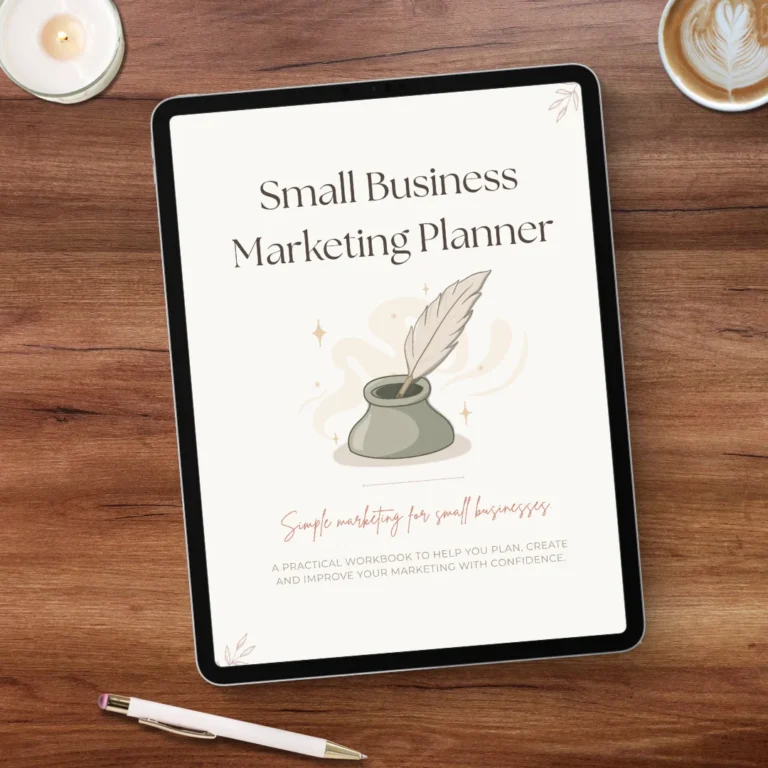 Small Business Marketing Planner displayed on a tablet, with a quill and inkpot cover illustration, beside a candle, coffee and pen on a wooden desk.
